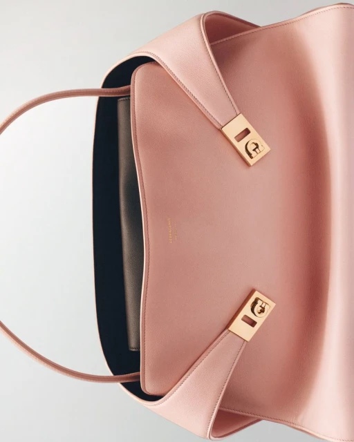 Pale pink Aigner tote bag with gold hardware and a black interior, photographed in portrait format with a high angle on a white backdrop.