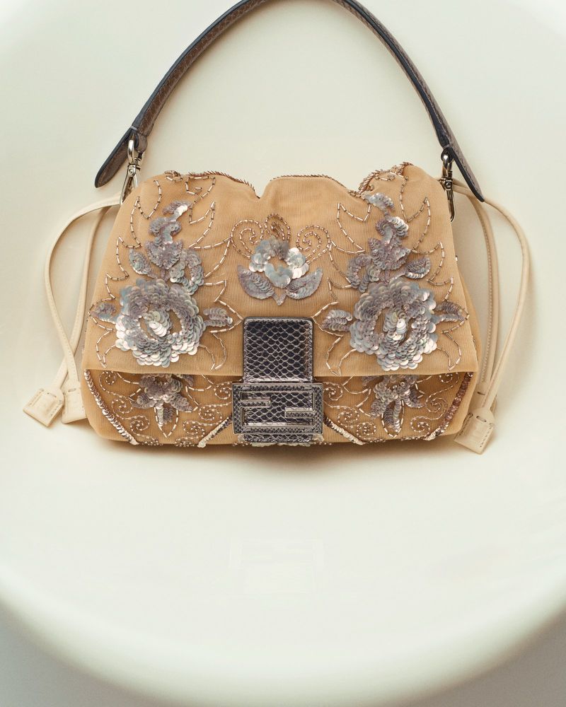 Tan Fendi Baguette handbag with floral sequin embellishments, a brown leather strap, and a cream-colored background.