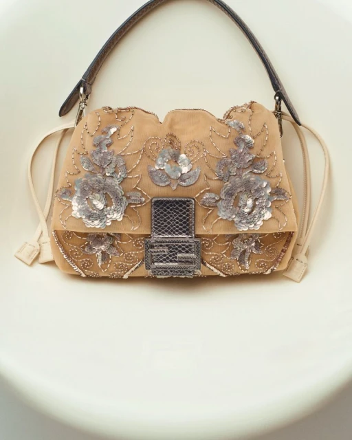 Tan Fendi Baguette handbag with floral sequin embellishments, a brown leather strap, and a cream-colored background.