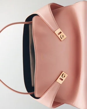 Close-up product shot of a pale pink leather handbag with gold hardware against a clean white background