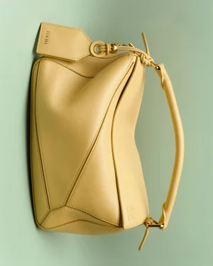 Yellow leather designer handbag featuring geometric paneling and a tag against a light green background.