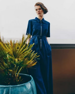 Model in a dark blue denim jumpsuit standing outdoors with a potted palm plant in the foreground by Tobias Delcroix for Grazia UK.