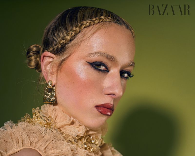 Close-up studio shot of a female fashion model with braided hair, dramatic makeup, and gold earrings wearing a ruffled collar.