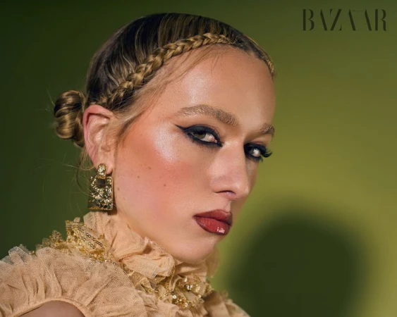 Close-up studio shot of a female fashion model with braided hair, dramatic makeup, and gold earrings wearing a ruffled collar.