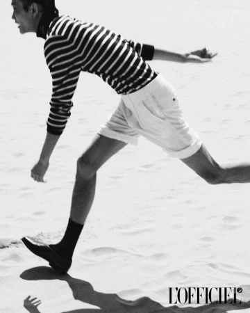 Model running on a sandy beach wearing a striped sweater and light shorts in a black and white fashion image