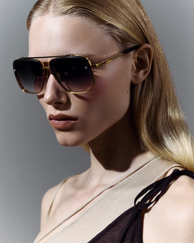 A woman with blond hair poses in a close-up shot wearing a pair of aviator sunglasses with a gold frame and gradient lenses.