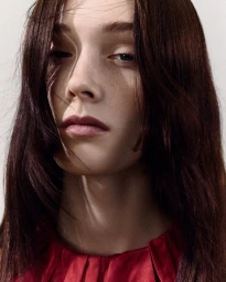 Close-up portrait of a woman with long dark hair wearing a red top against a white background
