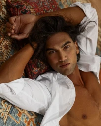 Model Chand Smith wearing an unbuttoned white shirt lying on an ornate patterned rug with arms behind head