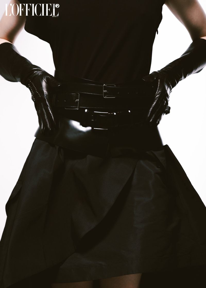 Cropped studio shot of a fashion model in a black top, black skirt, and long black gloves posing in front of a white background.