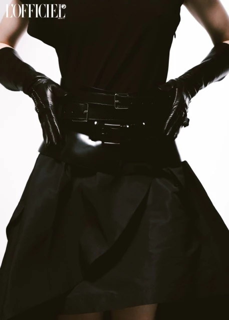 Cropped studio shot of a fashion model in a black top, black skirt, and long black gloves posing in front of a white background.