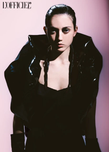 Fashion editorial portrait of a young adult woman wearing a black dress and a shiny black vinyl jacket with braided hair.