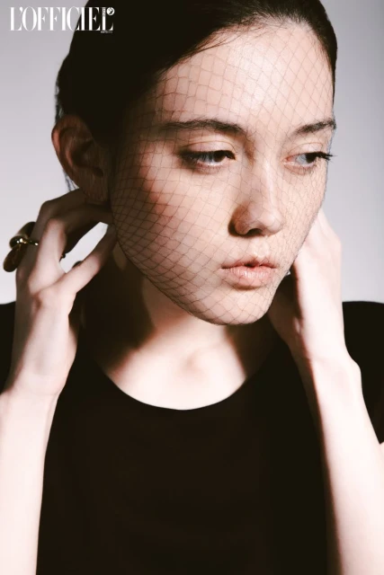 Close-up portrait of a young adult woman wearing a black top and a black net veil, studio lighting, beauty shot.