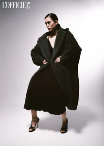 Model in dark green fluffy coat and black dress standing against a white studio background for L'Officiel Baltics