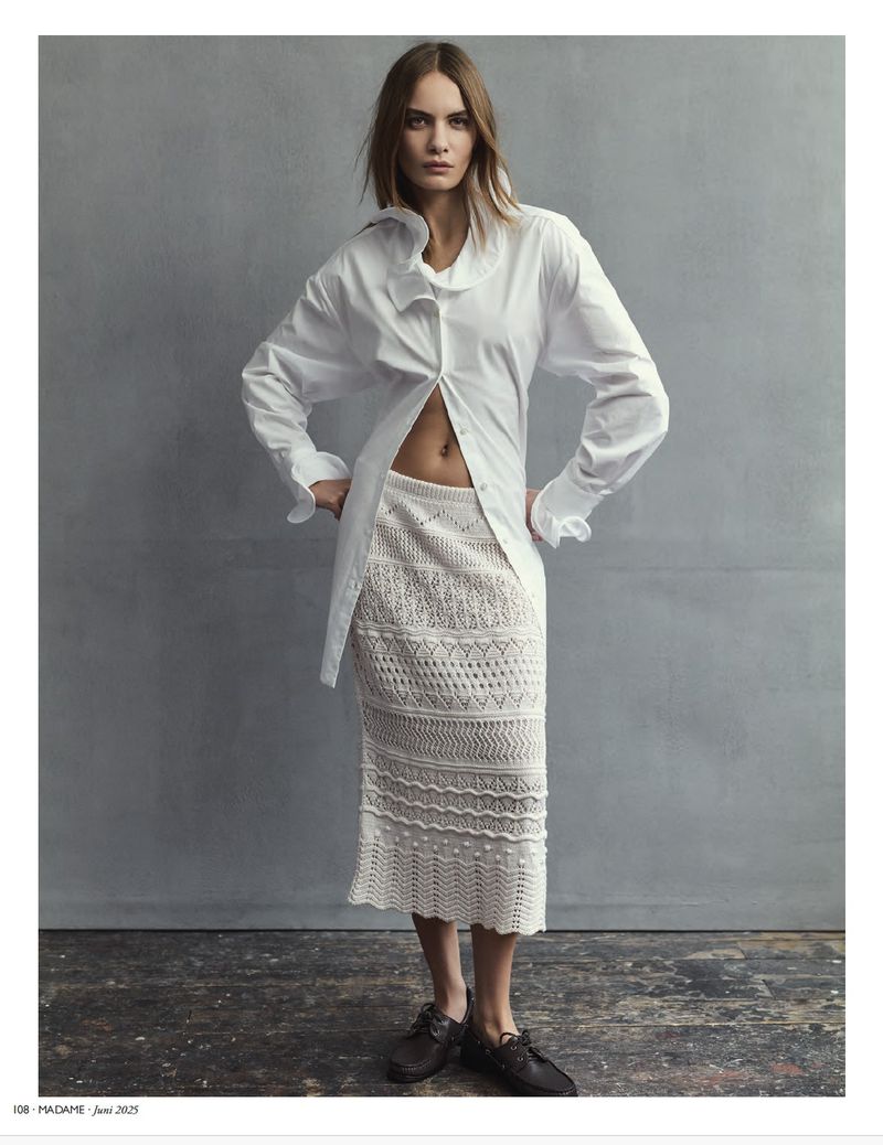Fashion shot of a woman posing in a white shirt and crochet skirt against a gray backdrop, showcasing a blend of textures and styles.