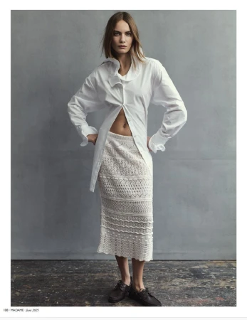 Fashion shot of a woman posing in a white shirt and crochet skirt against a gray backdrop, showcasing a blend of textures and styles.