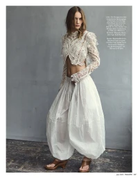 Model wearing white lace crop top and voluminous white trousers against a mottled grey wall.