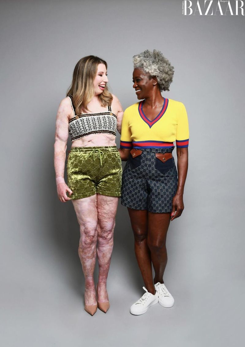 Two women pose in a photo studio wearing summer outfits. The fair-skinned woman wears green velvet shorts and the Black woman wears patterned shorts.