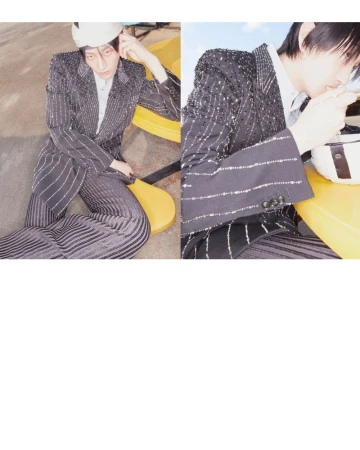 Editorial fashion shot: androgynous model in a striped suit with a white cap, sitting on a yellow chair in an indoor setting.