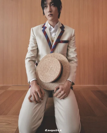 Portrait of adult male kneeling indoors with straw hat in hands and wearing white jacket and pants and striped shirt collar.
