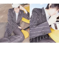 Model Hamin Yu wearing a dark embellished suit and patterned trousers, seated outdoors on yellow seating.