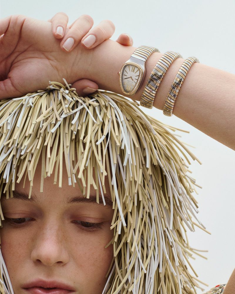Close-up of a woman wearing a gold Bulgari Serpenti Seduttori watch with a snake-like band, complemented by a unique straw-like wig.