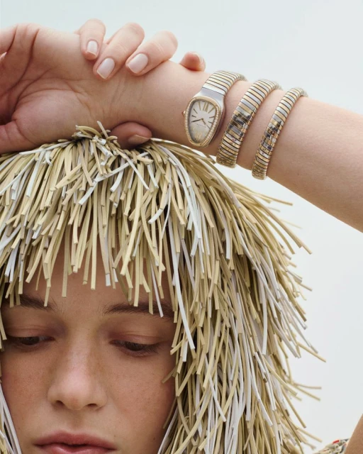 Close-up of a woman wearing a gold Bulgari Serpenti Seduttori watch with a snake-like band, complemented by a unique straw-like wig.
