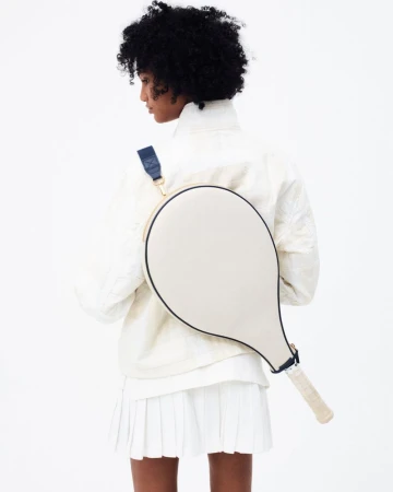 Back view of a dark-haired woman with a tennis racquet on her back wearing a white jacket and skirt, against a white backdrop.