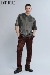 Model wearing a glossy green silk t-shirt and brown trousers against a white studio background