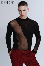 Male model wearing a sheer black long-sleeve top and red trousers against a plain light grey background