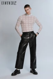 Male model with short hair wearing a sheer patterned turtleneck and black leather trousers against a pale grey background.