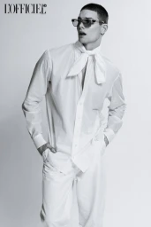 Monochrome fashion portrait of a male model wearing a white shirt with a necktie and trousers against a white backdrop.