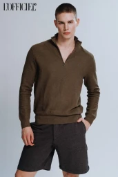 Young male model wearing an olive green quarter-zip sweater and dark grey shorts against a pale background for L'Officiel Baltics.