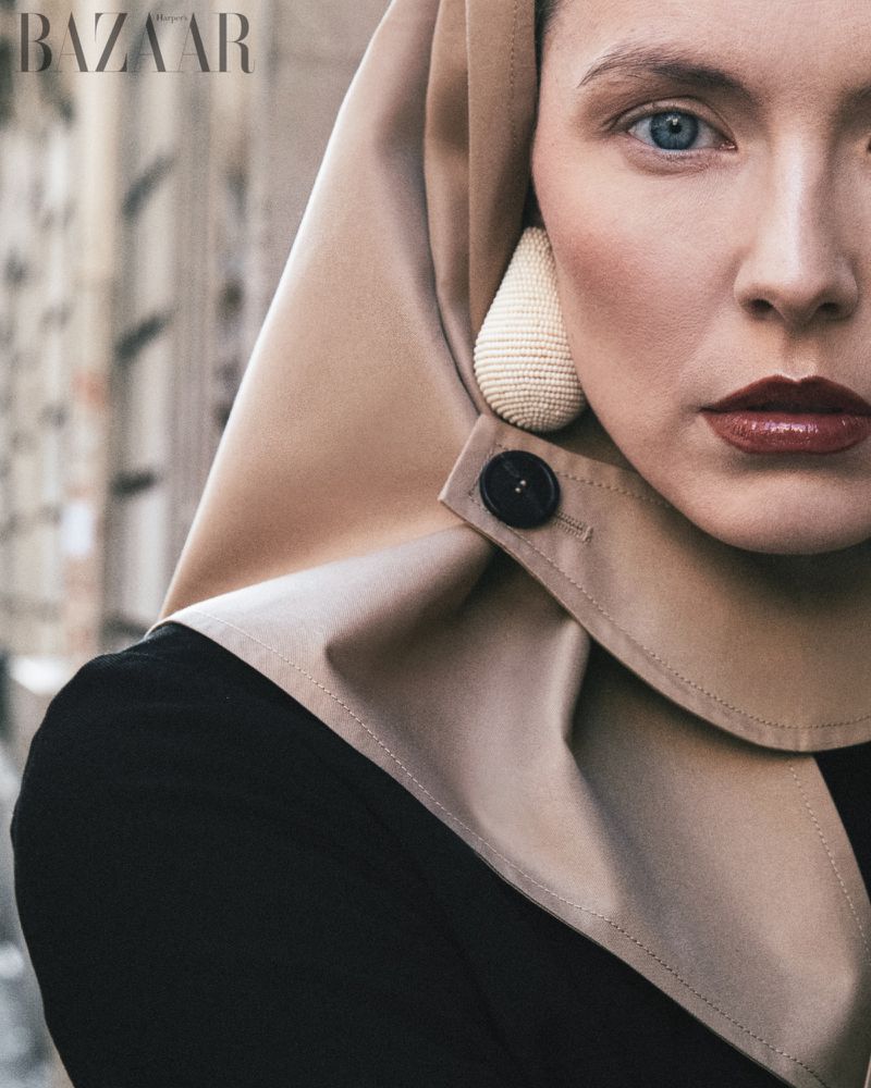 Close-up of a woman with blue eyes wearing a hooded garment with a button, complemented by large earrings and striking red lipstick.