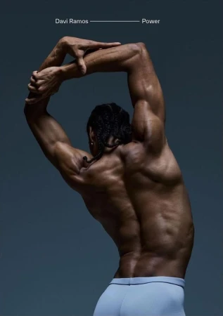 Muscular adult male, photographed from the back, in an artistic studio shot against a gray background, showcasing fitness and strength.