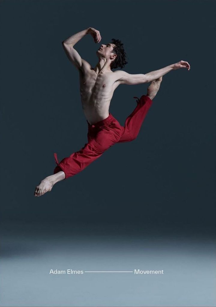 A male ballet dancer in mid-air leap, captured in a dynamic full shot against a blue background in a photo studio setting.