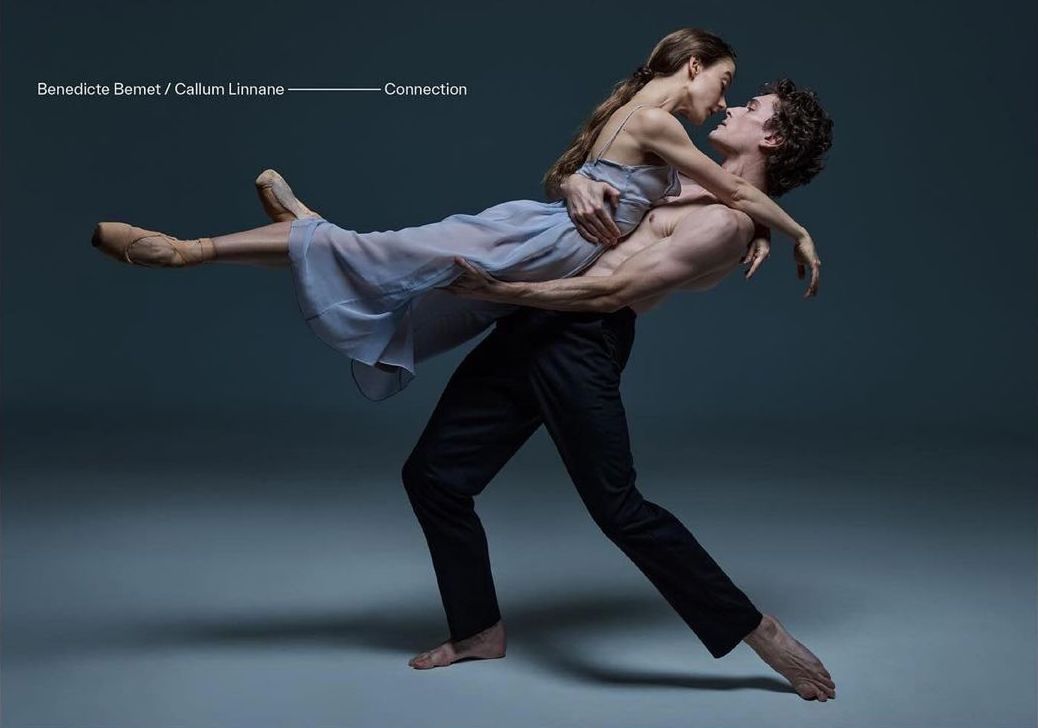 A male dancer holding a female ballet dancer close, set against a muted grey backdrop, showcases a moment of connection and artistry.