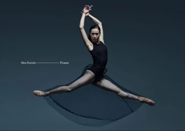 Ballet dancer Ako Kondo leaping mid-air in a black leotard and sheer skirt against a dark grey background for the Australian Ballet.