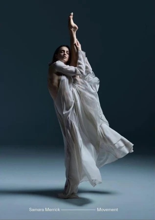 A woman in a flowing white dress gracefully balances on one leg while extending the other leg straight up in a balletic pose.