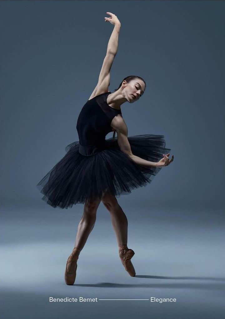 Elegant full-length portrait of a ballerina in a black tutu gracefully posing on a solid grey background with pointe shoes.