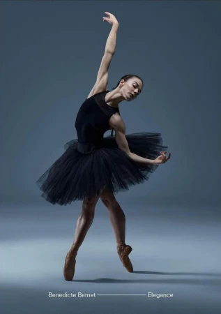Elegant full-length portrait of a ballerina in a black tutu gracefully posing on a solid grey background with pointe shoes.