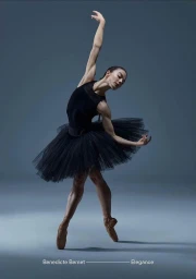 Ballet dancer in a black tutu and point shoes posing mid-performance against a solid dark grey studio background.