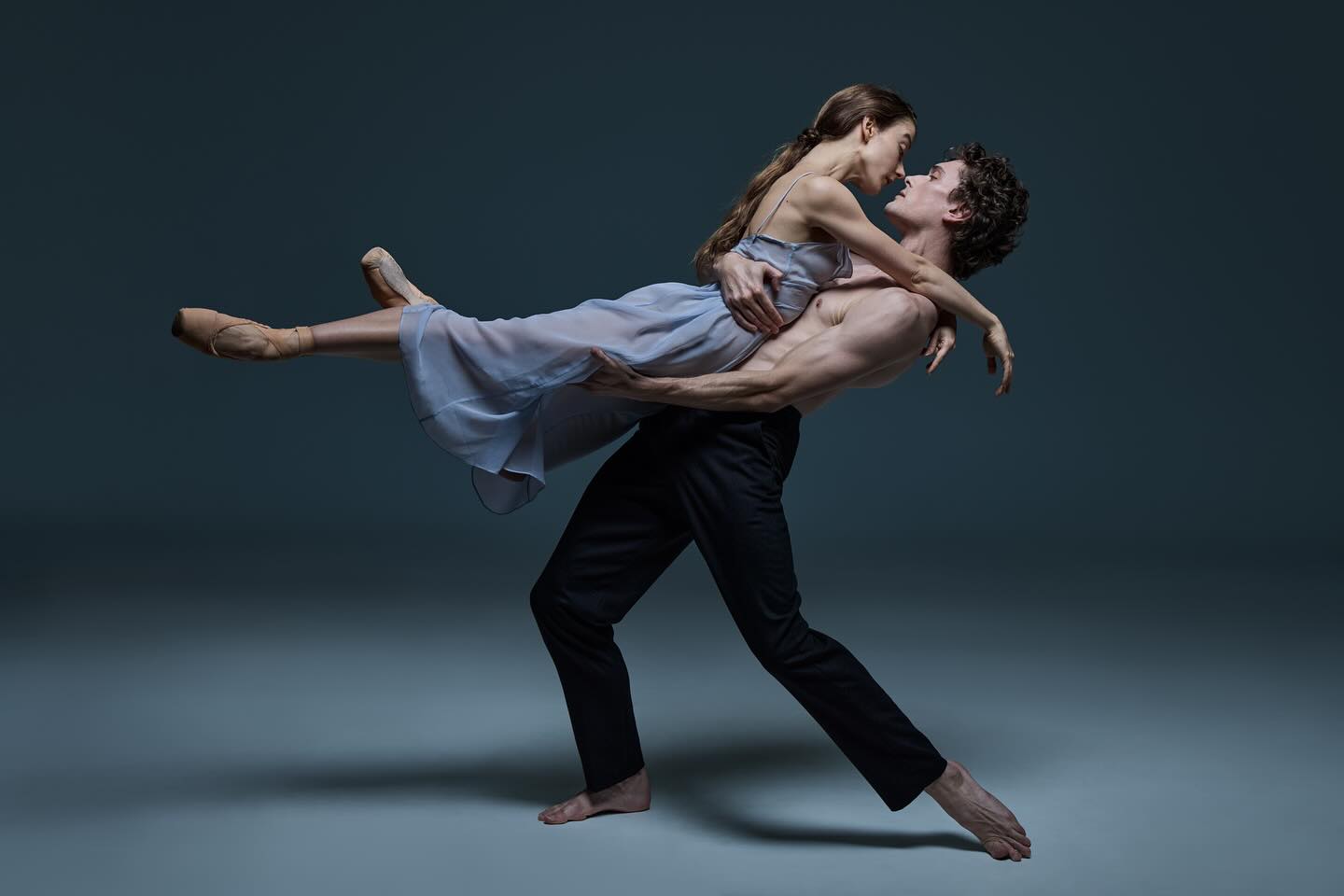 Elegant ballet dancers strike a pose in a studio; a muscular male dancer lifts the female dancer as they share a kiss.