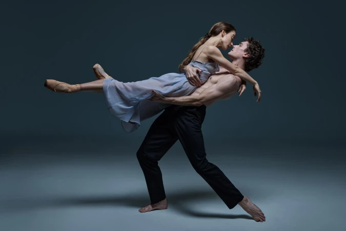 Elegant ballet dancers strike a pose in a studio; a muscular male dancer lifts the female dancer as they share a kiss.