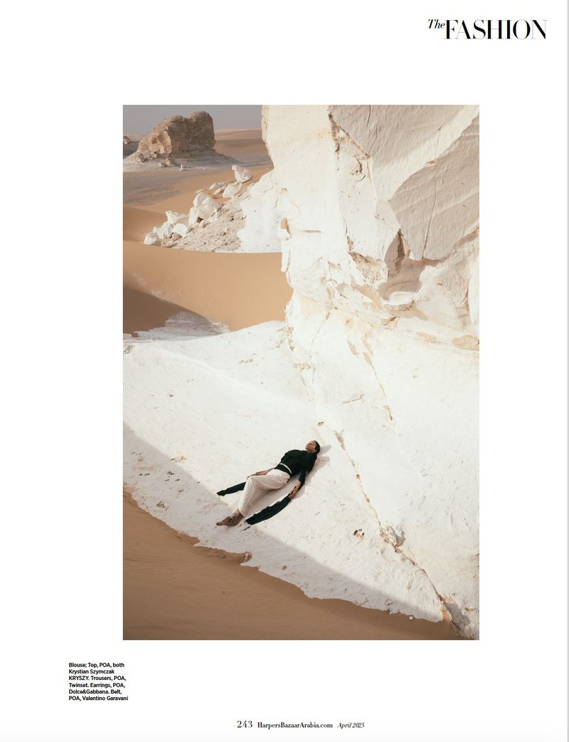 Fashion editorial shot of a woman lying on white rocks in the desert, wearing a dark top and light-colored pants, under natural sunlight.