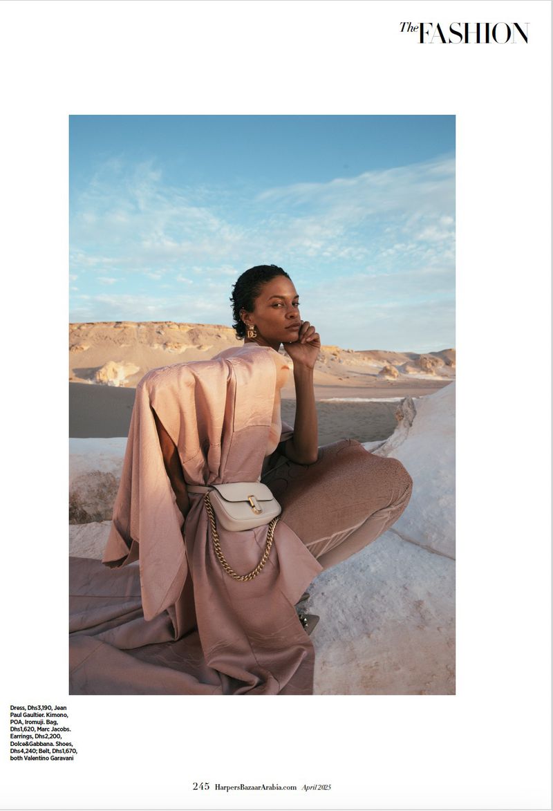 Fashion editorial shot: a woman in a flowing beige outfit poses in the desert against a blue sky, showcasing a modern, elegant aesthetic.