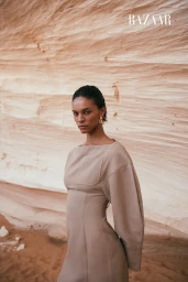 Model in a beige dress standing against a textured rock formation background for Harper's Bazaar Arabia Open Plan