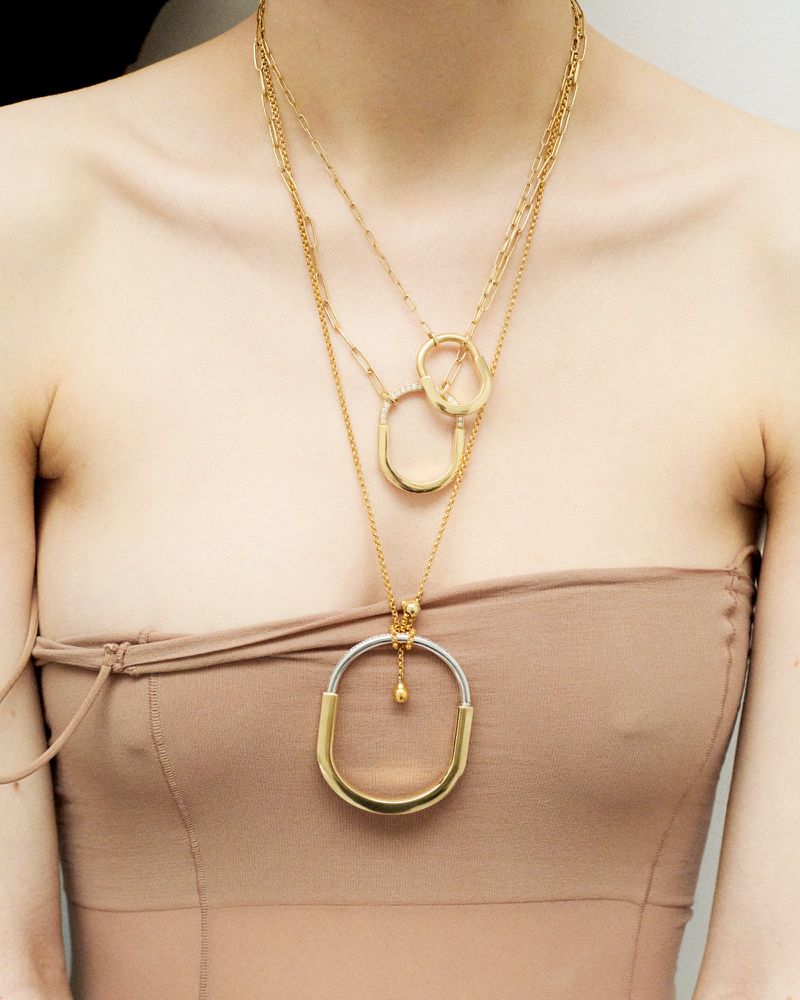 A woman with fair skin wears a strapless dress and multiple layered gold necklaces featuring different shapes and sizes of pendants.
