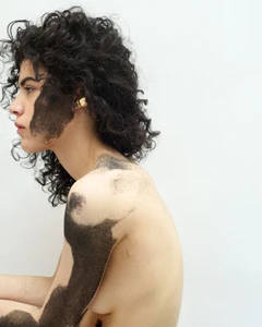 Model with dark curly hair and face markings photographed against a white background for Puss Puss Magazine