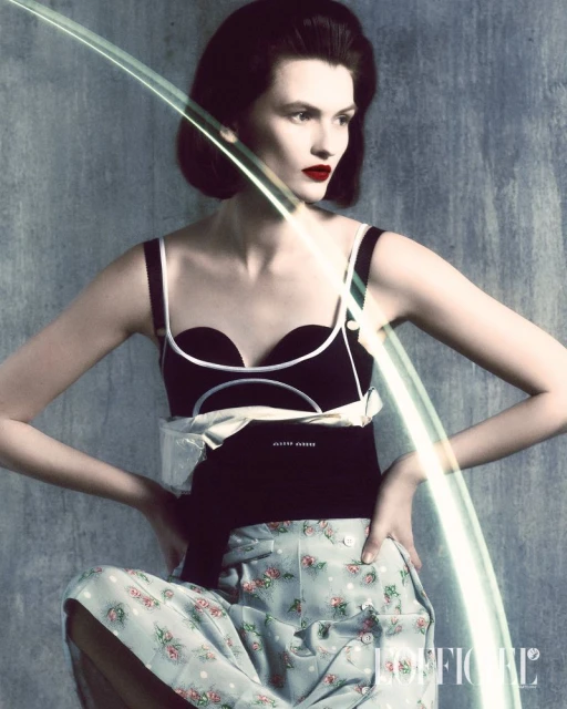 Elegant woman in black top and floral pants posing with light effects against a grey backdrop in a fashion editorial style.
