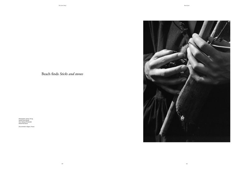 Monochrome capture of hands holding twigs and a stone, set against a dark fabric backdrop in a composition evoking editorial style.